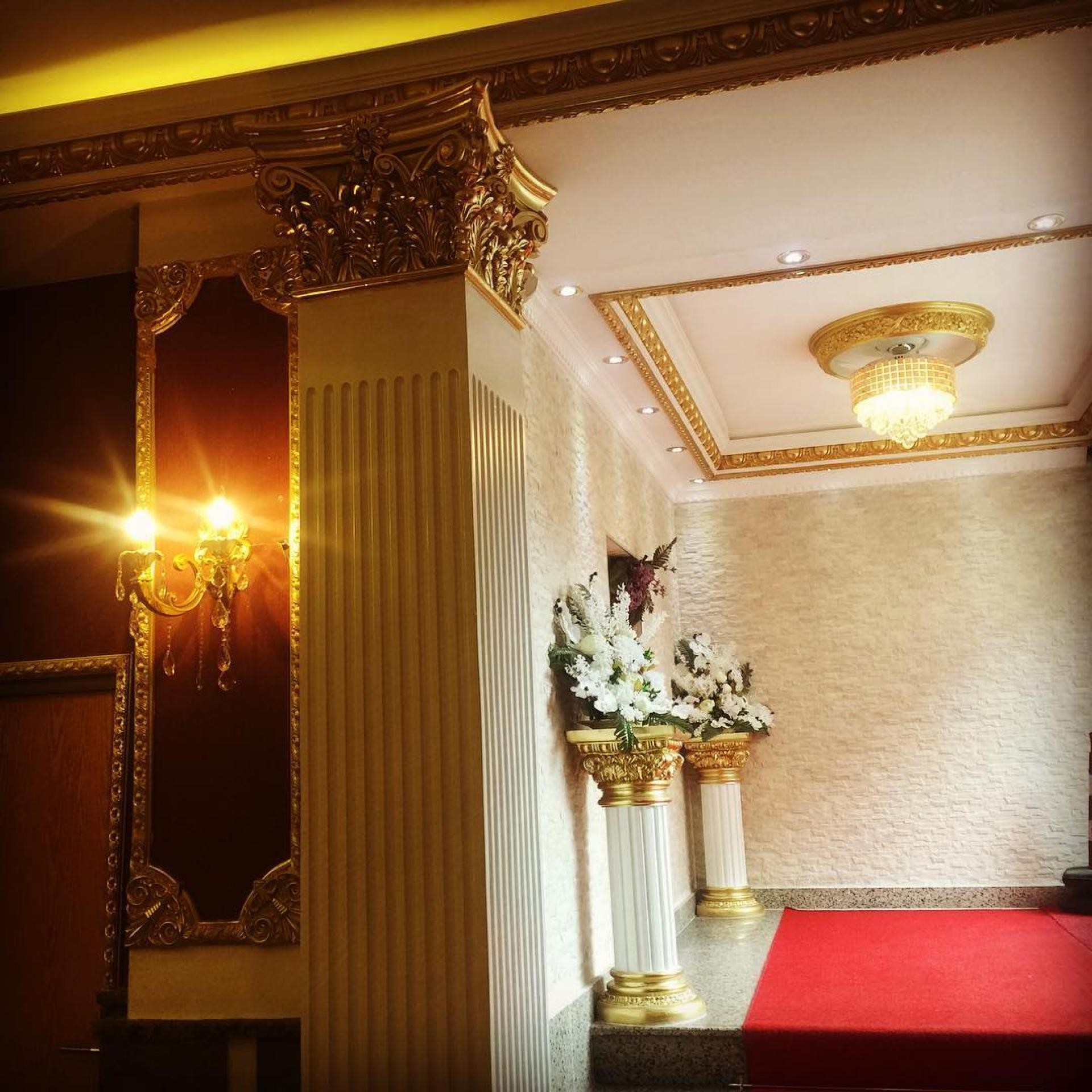 Kırmızı halılı bir mekan girişinde altın varak işlemeli poliüretan pilaster sütun, duvar aplikleri ve tavan dekorasyonu.