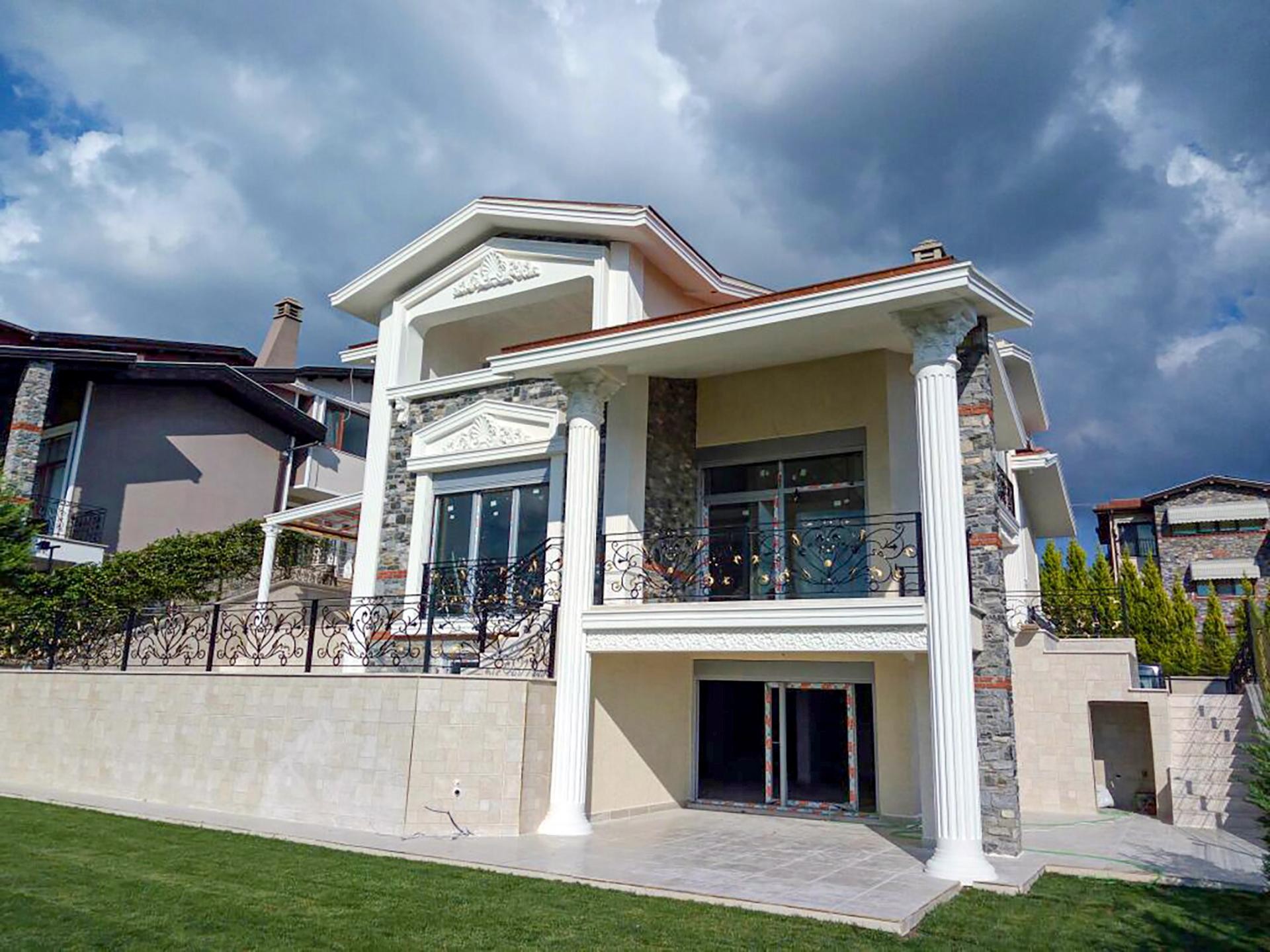 Doğal taş kaplamalı ve beyaz renkli dış cepheye sahip, pencerelerinde poliüretan üçgen taçlar ve söveler, balkonunda dairesel poliüretan sütunlar bulunan üç katlı villa.