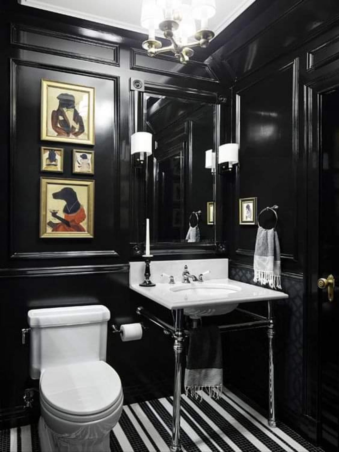 Parlak siyah boyalı banyo duvarında poliüretan çıta çerçeveleri içinde hayvan figürlü tablolar, krom ayaklı beyaz lavabo, tuvalet ve çizgili zemin.