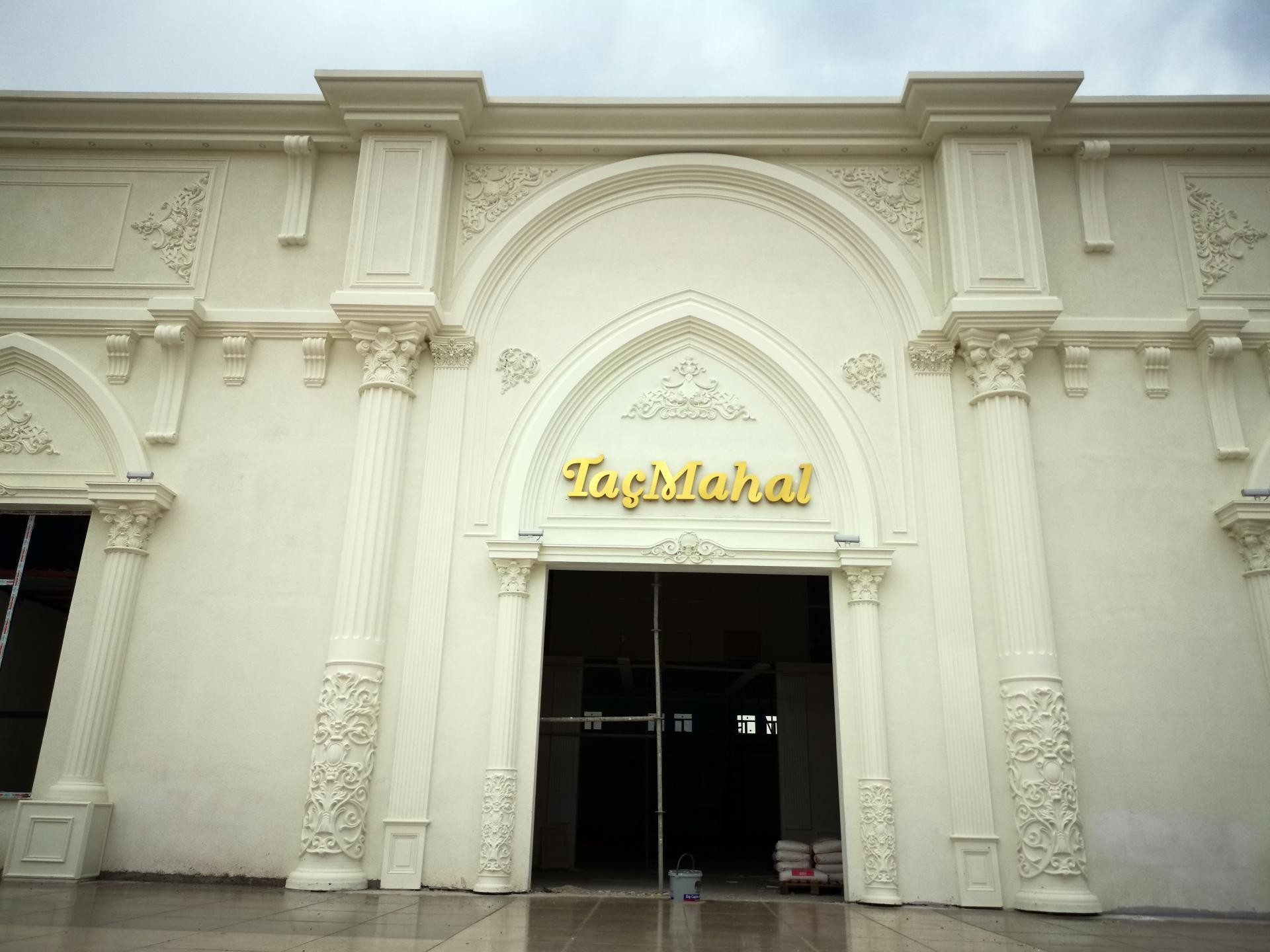 "TaçMahal" yazılı ana girişi bulunan, krem renge boyanmış, poliüretan pilaster sütun, kemer ve kabartmalarla kaplı büyük etkinlik binası cephesi.