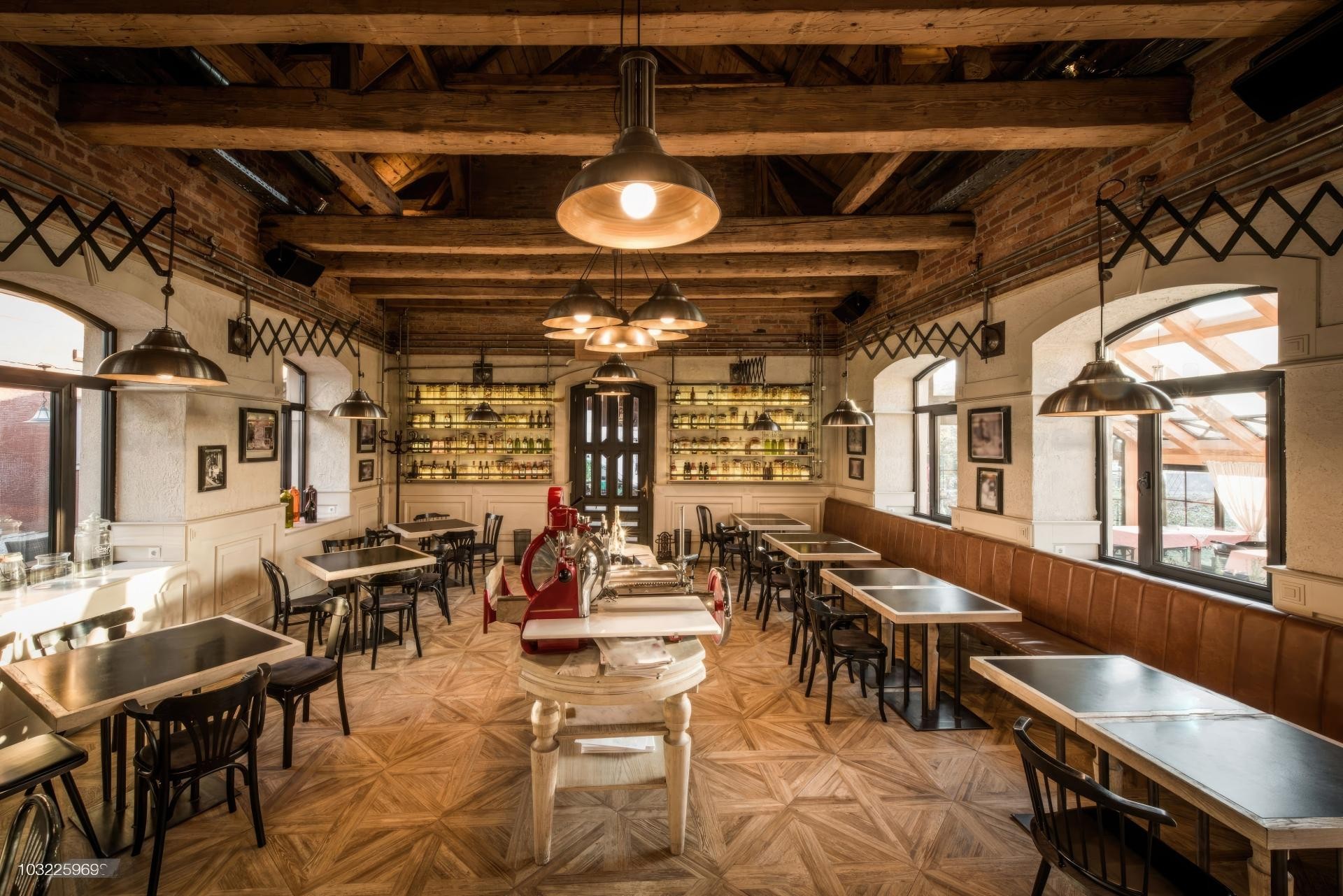 Simetrik açıyla çekilmiş restoran iç mekanında, tavanda çapraz kurgulanmış poliüretan ahşap taklidi kütükler, endüstriyel sarkıt lambalar, tuğla duvarlar ve ahşap masa sandalyeler.