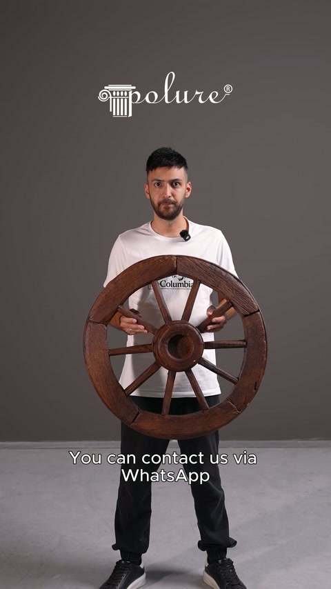 Sunucu stüdyoda ahşap görünümlü dekoratif araba tekerleğini gövdesi önünde tutuyor