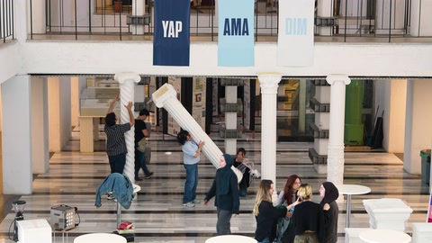 Katılımcılar atriyumdaki büyük dekoratif parçanın kurulumuna yardım ediyor