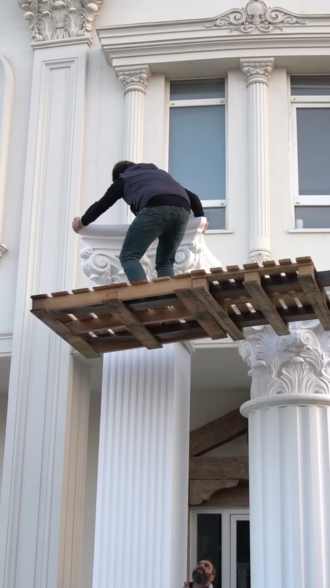 Çömelmiş usta geniş Korint başlığını sütunlar arasındaki platformda düzeltiyor.