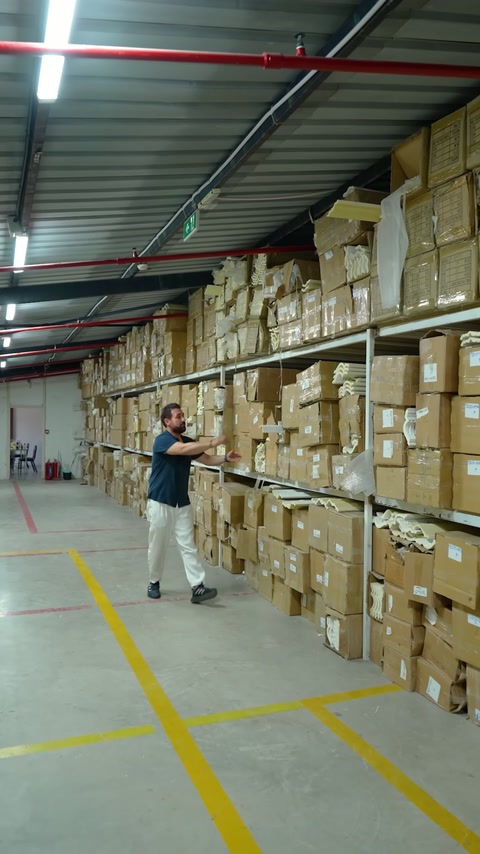 Tasarımcı, geniş depoda kutulu stoklar ve dekoratif profiller arasında ilerliyor.