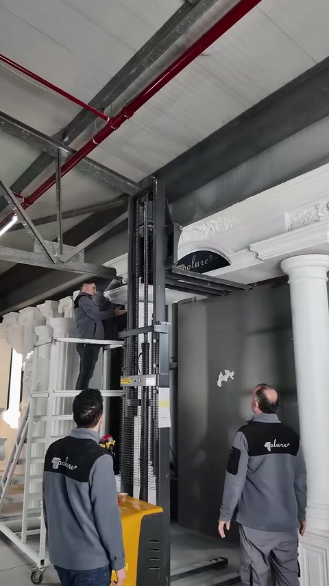 İki çalışan, yükseltilmiş taç elemanının yerleşimini aşağıdan izliyor.
