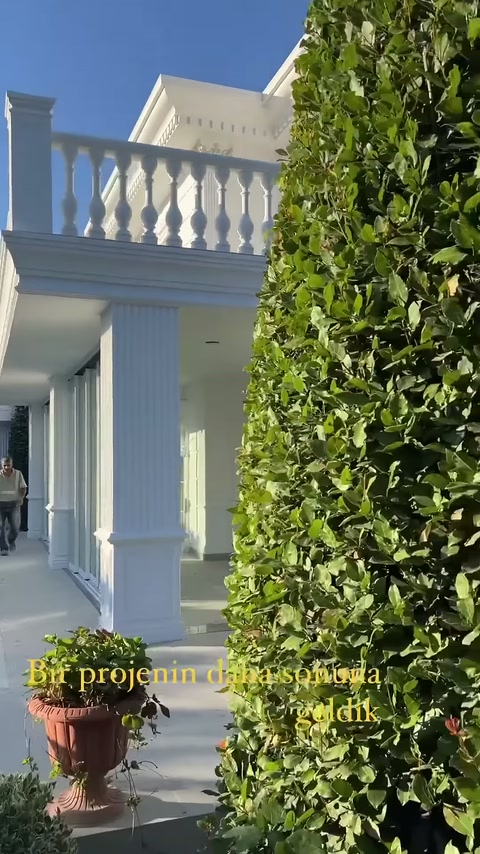 Biçimli çit arkasında villanın korkuluklu balkonu ve sütunlu terası seçiliyor.
