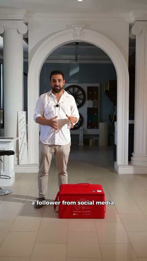 Sunucu showroom ortamında yerdeki kırmızı taşıma çantasını tanıtıyor.