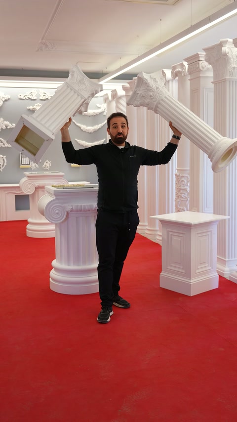 Sunucu, sergi alanında kemer ve sütun parçalarını iki eliyle gösteriyor