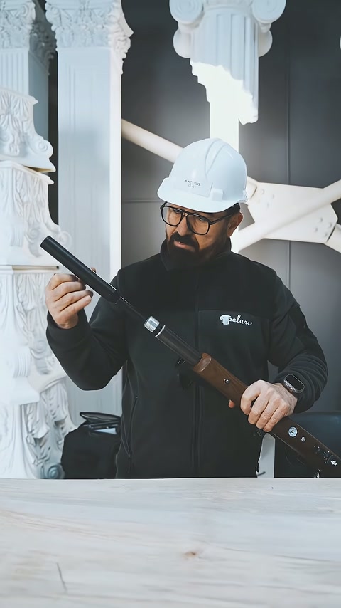 Usta, beyaz dekoratif sütunların önünde test tüfeğini kontrol ediyor.