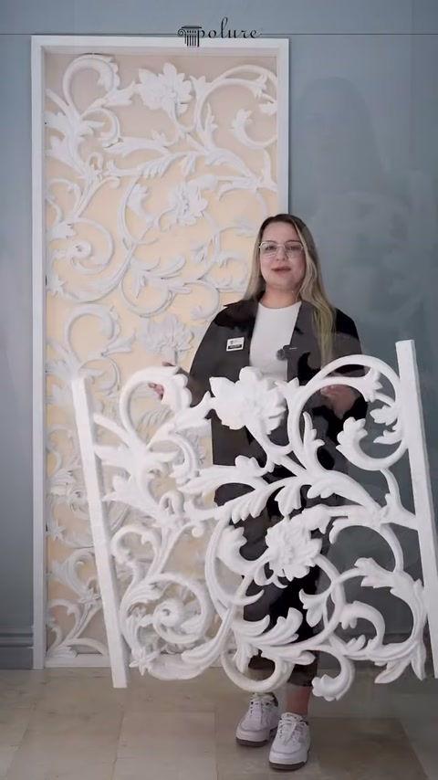 Sunucu, beyaz bitkisel desenli dekoratif paneli sergi alanında tutuyor