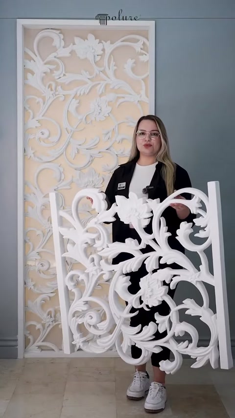 Sunucu, kıvrımlı sarmaşık desenli paneli iki eliyle sergiliyor