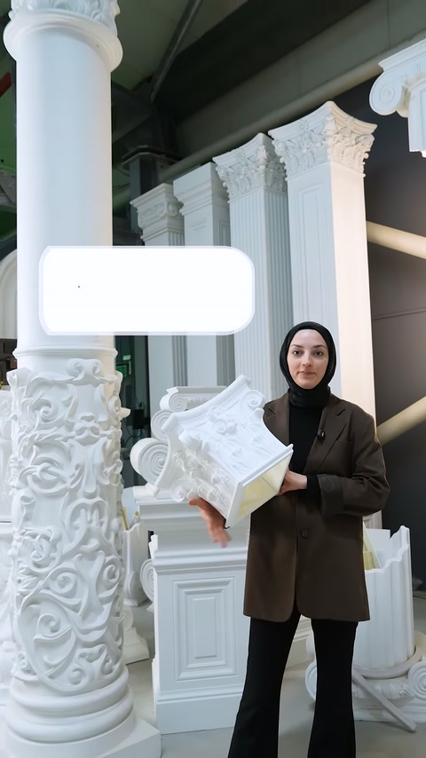 Sunucu elinde bezemeli beyaz sütun başlığı numunesini tutarak konuşuyor
