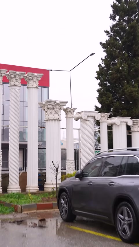 Bina dış cephesinde sütunlu giriş ve park halindeki araç görülüyor