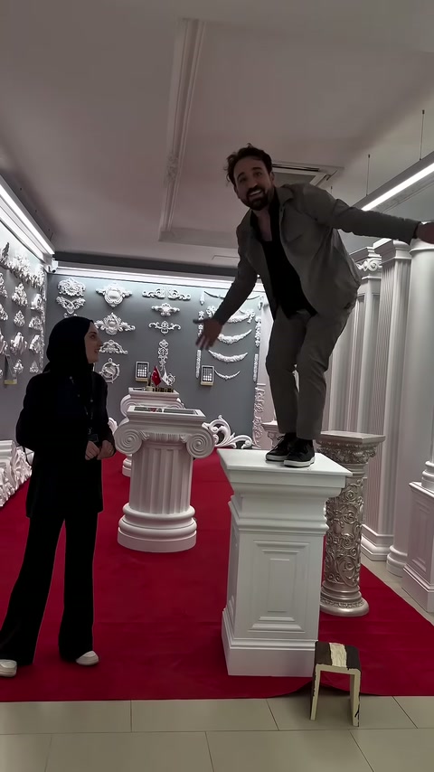 Tanıtıcı, tablasında erkek bulunan kare sütun sehpanın yanında bekliyor.