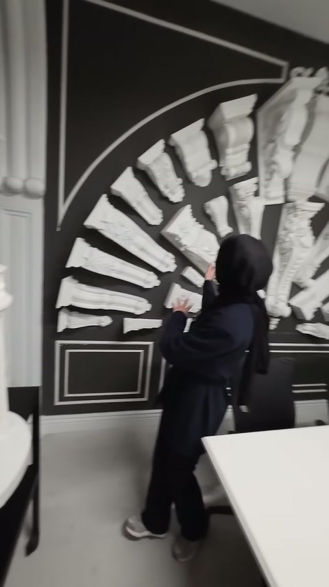 Siyah sergileme duvarında çeşitli beyaz dekoratif payandalar ışınsal düzende sunuluyor.