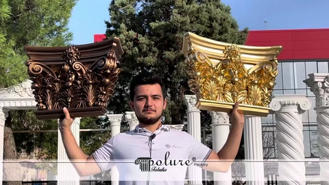 Görevli iki süslü sütun başlığını omuz hizasında yakından sergiliyor