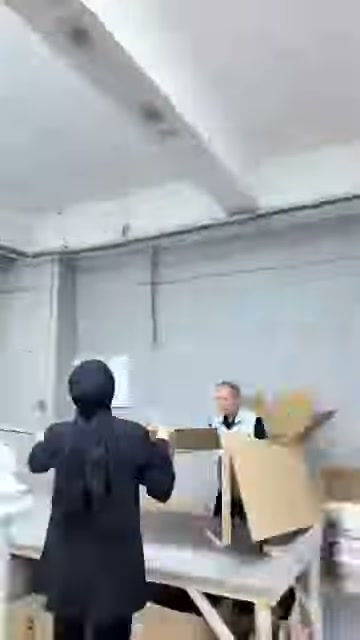 İki kişi, geniş karton levhayı paketleme bölümüne taşıyor.