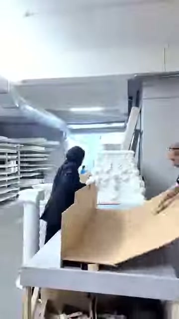 Açık karton kutu, paketleme masasındaki beyaz parçaların önünde duruyor.