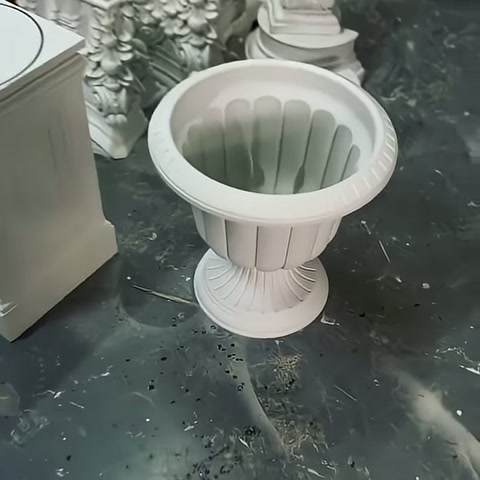 Beyaz oluklu saksı gövdesi, üretim alanında yuvarlak ayağı üzerinde duruyor.