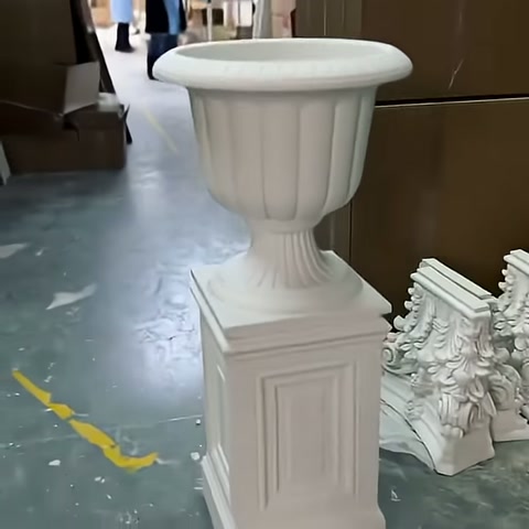 Tamamlanan beyaz dekoratif saksı, üretim alanındaki süslemeler önünde sergileniyor.
