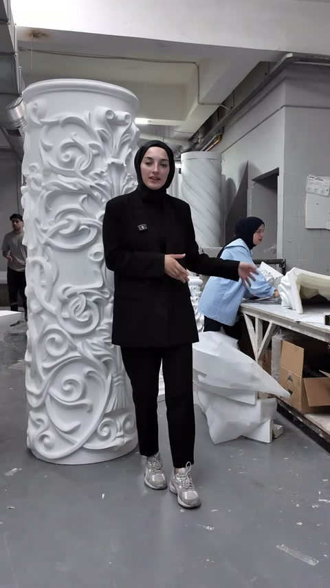 Sunucu atölyede yoğun bitkisel kabartmalı geniş sütun gövdesinin yanında duruyor.