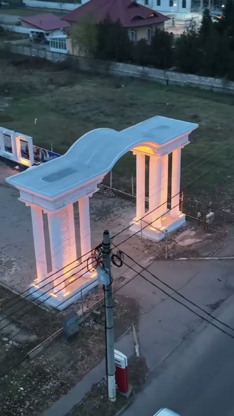 Dalgalı başlıklı dekoratif giriş, yol kenarında aydınlatılmış sütunlarla görülüyor