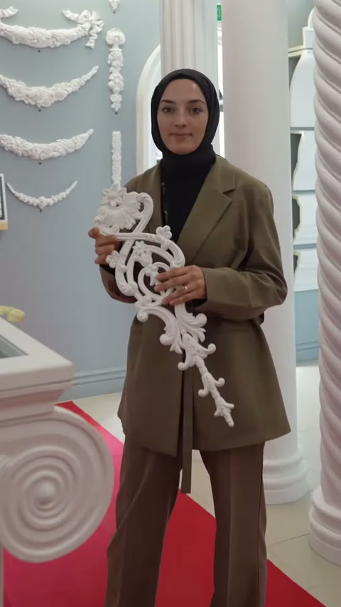 Sunucu showroomda büyük beyaz kıvrımlı motif parçasını dikey tutuyor
