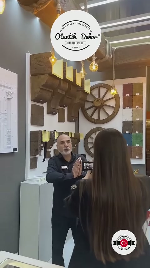 Tavan kirişleriyle düzenlenen stantta sunum yapan görevli ve ziyaretçi görülüyor