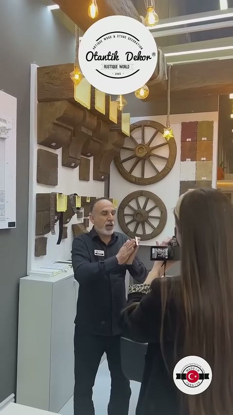 Görevli sergi alanındaki koyu renkli kiriş örneklerini ziyaretçiye tanıtıyor