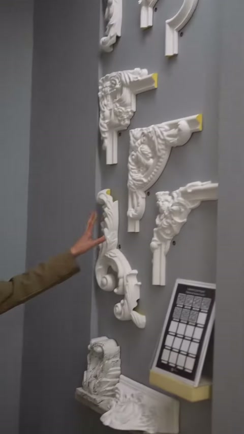 Gri showroom duvarındaki poliüretan köşe motifleri elle işaretleniyor.
