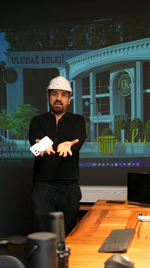 Uzman, okul cephesinin tasarım görseli önünde proje anlatıyor.