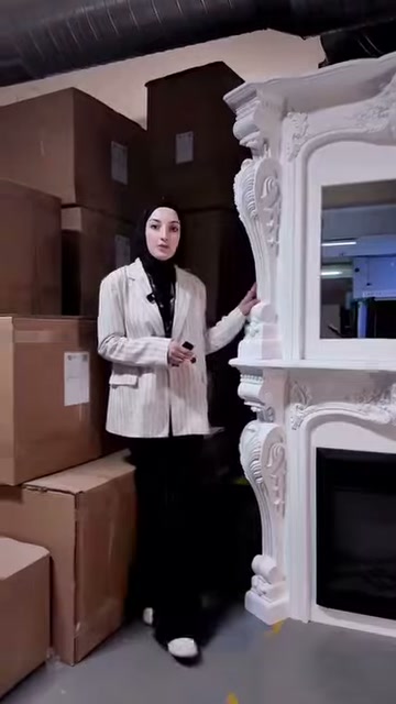 Sunucu kıvrımlı yan süslemelere sahip şöminenin yanında duruyor