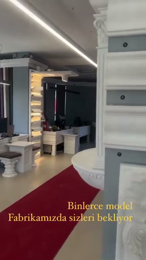 Beyaz dekoratif sütun yanında kırmızı halılı showroom geçişi bulunuyor
