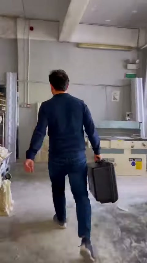 Görevli, cihaz çantasını taşıyarak atölyenin çalışma bölümüne doğru yürüyor.