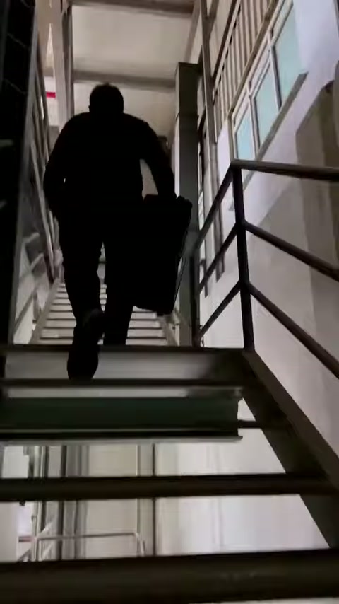 Ekipman çantalı görevli, üretim alanındaki metal merdivenlerden yukarı çıkıyor.