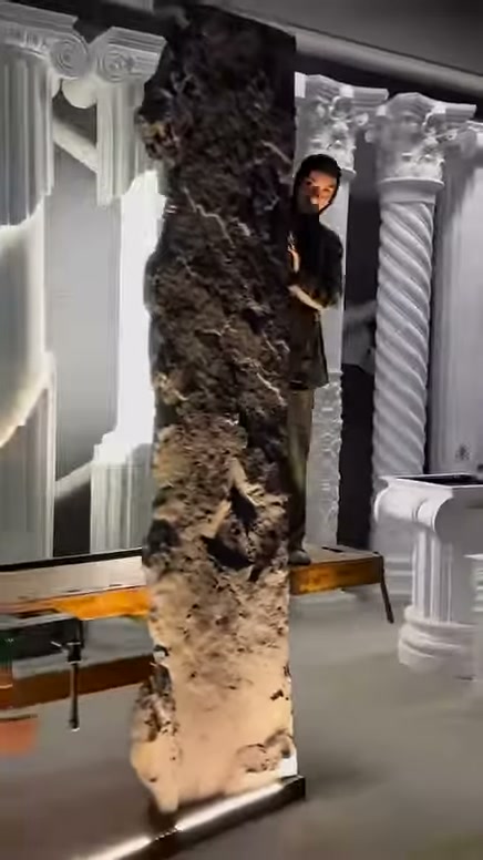 Dikey kaya panelinin düzensiz yüzeyi showroom aydınlatması altında sergileniyor