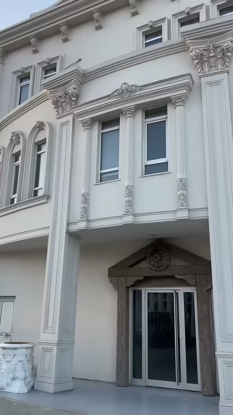 Beyaz bina cephesinde sütunlu pencere düzeni ve profilli silmeler görülüyor