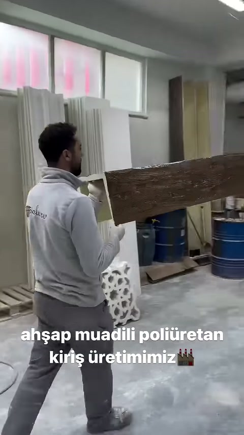 İki çalışan uzun rustik mertek profilini atölyede taşıyor.