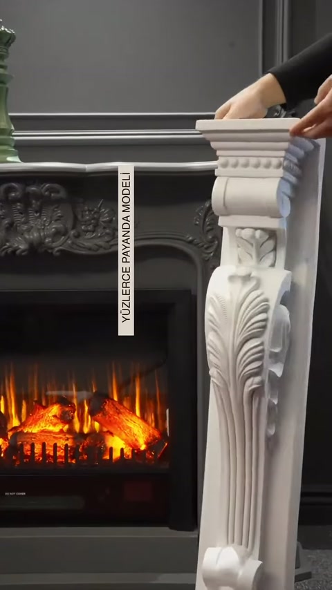 Beyaz dekoratif şömine payandası, gri ateş efektli şömine önünde tutuluyor.